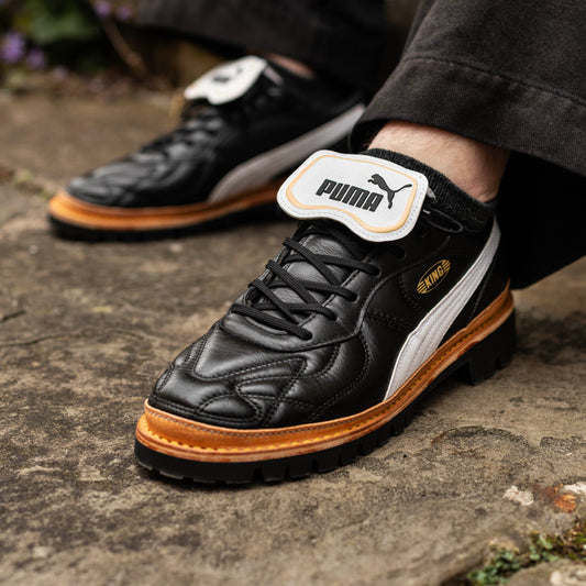 Black and white sneakers with orange soles on a stone surface, featuring a brand logo.